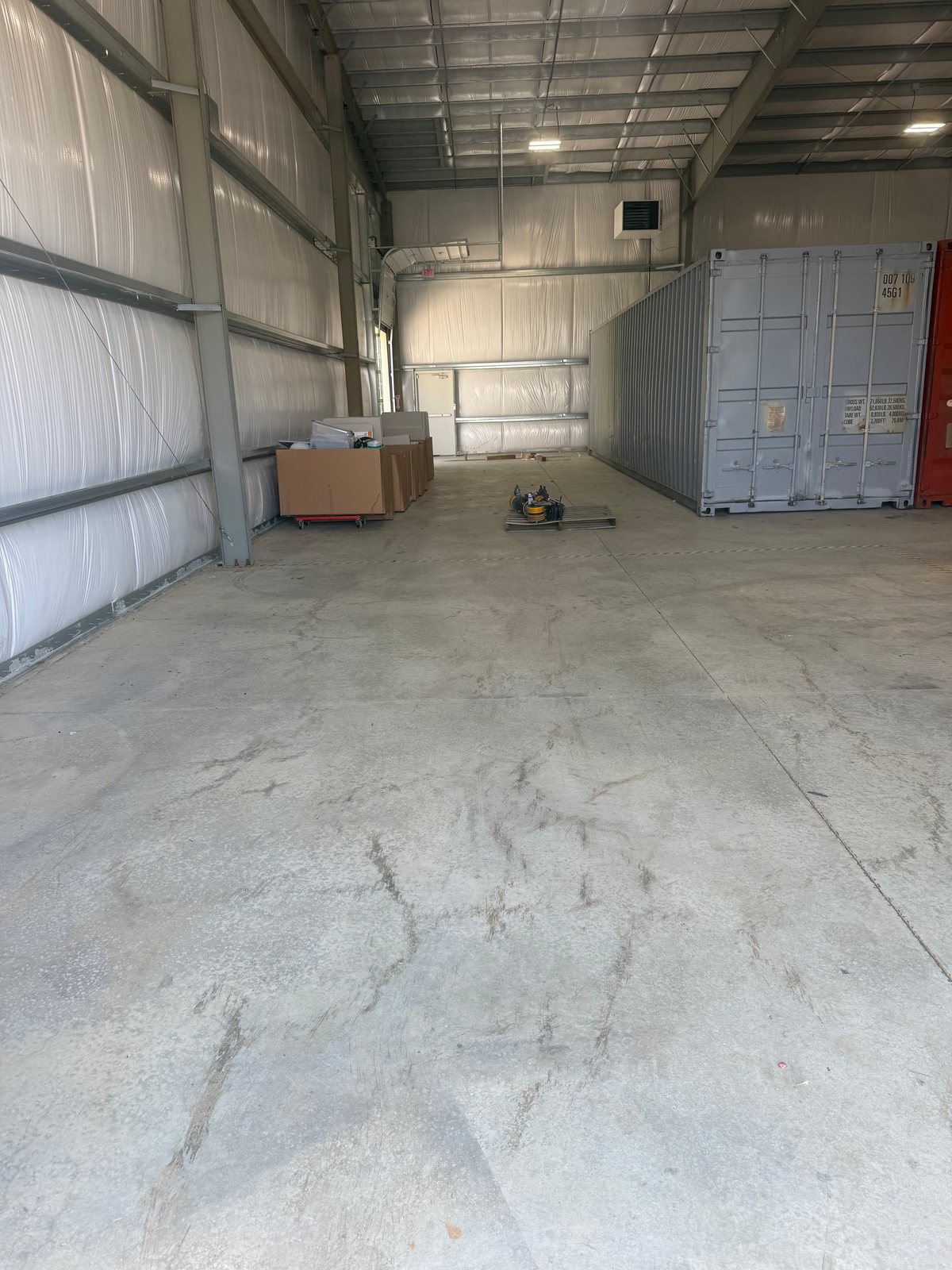 The Flat Rate Movers warehouse — interior with a grey shipping container on the right, boxes on a dolly on the left and equipment on a pallet in the centre